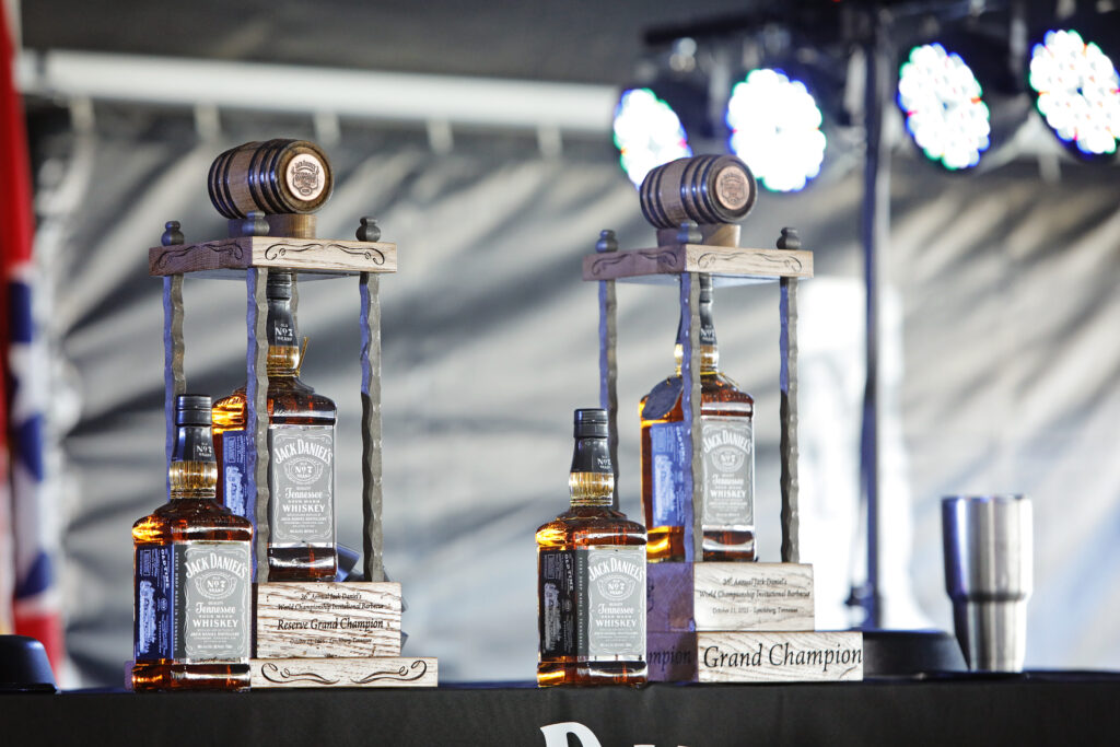 Two Jack Daniel's bottles displayed as trophies on a stage. Each bottle is flanked by a wooden frame with a gavel on top, labeled "Grand Champion."